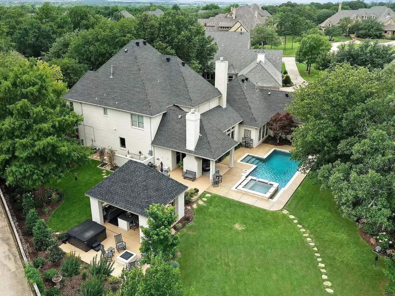 Aerial drone view of a premium Decra Shake XD stone-coated steel roof replacement in progress on a luxury estate in Denton, TX — RoofDog crew on roof with branded basketball court visible